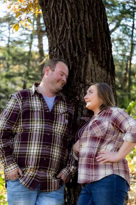 Portrait of a man and woman leaning up against a tree looking into each others eyes